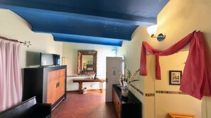 A room with a television, a mirror, a wooden cabinet, a bench, and a red curtain. - Hotel Utopía (Benalup-Casas Vieja)