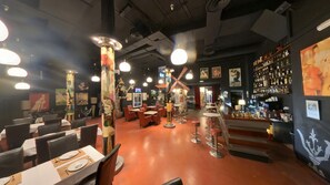 Un restaurante con mesas y sillas, una zona de bar y varias obras de arte en las paredes.