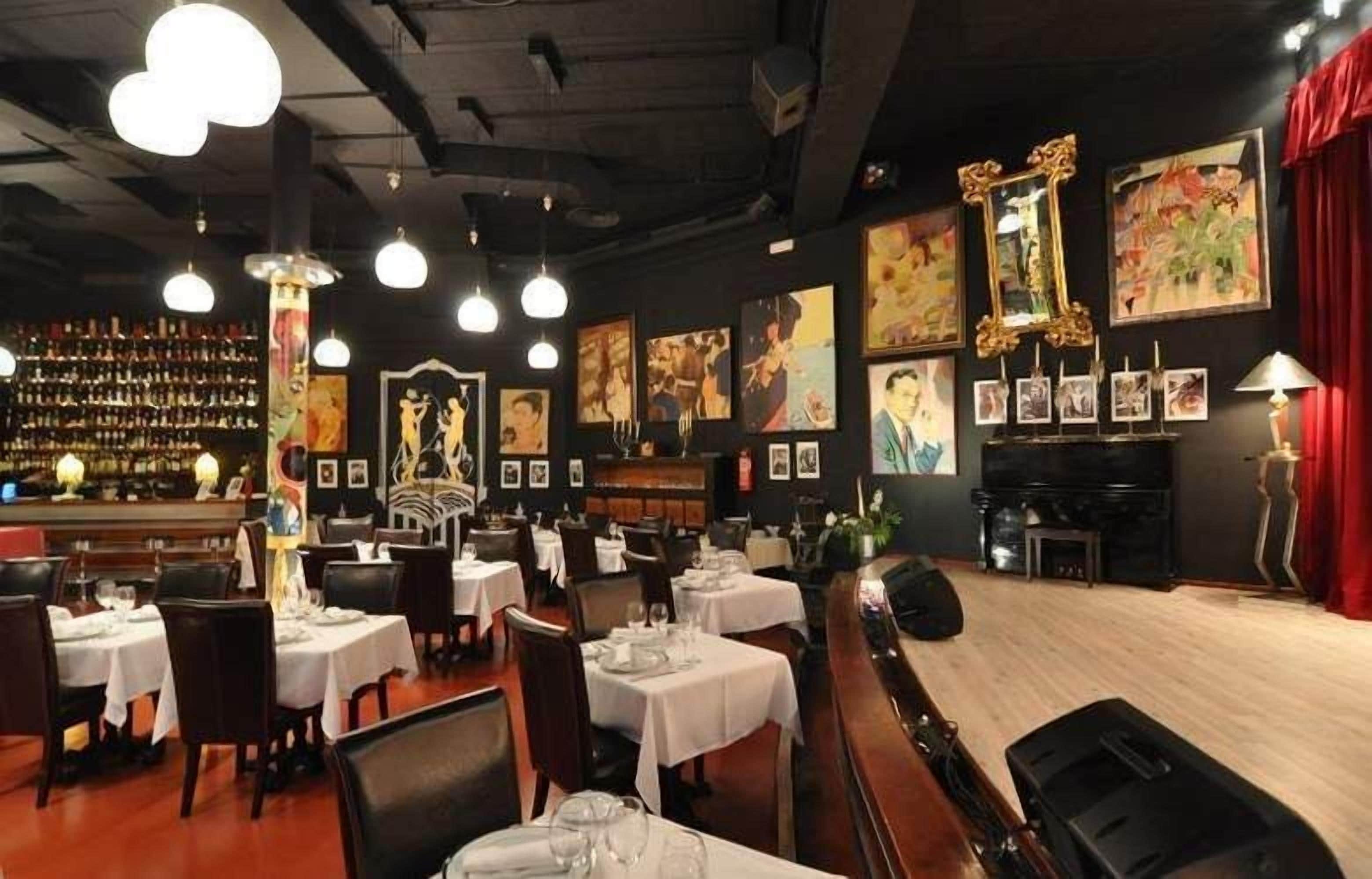Un restaurante con mesas preparadas para comer, una zona de bar y obras de arte en las paredes.
