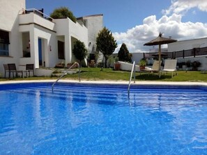 A swimming pool with a clear blue water surface, surrounded by white buildings, a grassy area, and a few lounge chairs. - Hotel Utopía (Benalup-Casas Vieja)