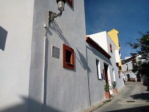 A narrow street with white buildings, a street lamp, and potted plants.
