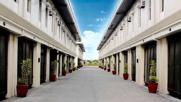A long, straight corridor with potted plants on either side, leading to a building with large windows and doors. - Executive Lofts by Mystique Lane (Bacolor)