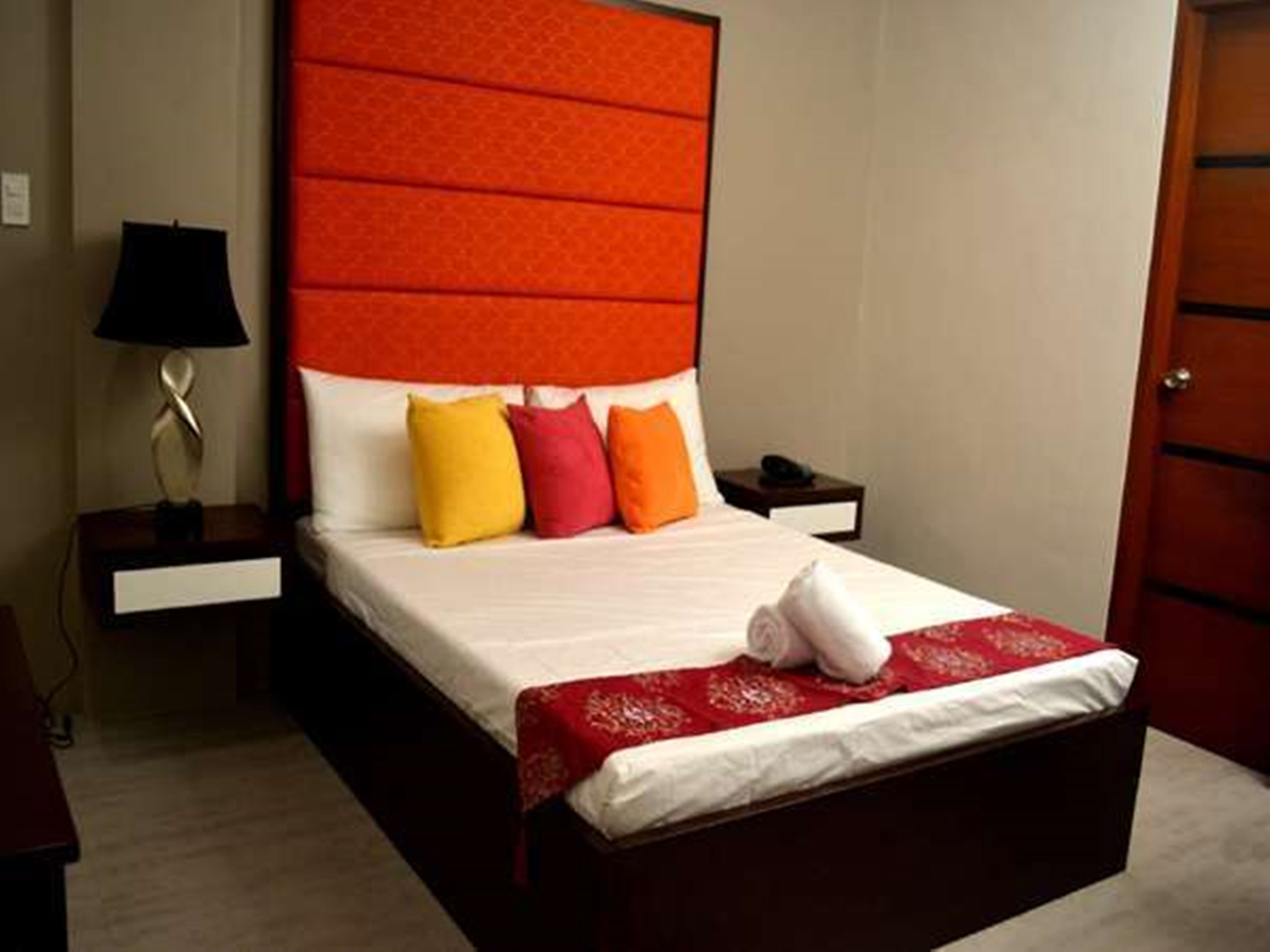 Una habitación de hotel con una cama grande, una mesita de noche con lámpara y una puerta de madera.