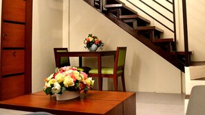 A staircase with wooden steps and a handrail, a wooden table with a vase of flowers, and a green chair. - Executive Lofts by Mystique Lane (Bacolor)