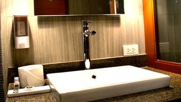 A bathroom with a rectangular sink, a mirror, a towel dispenser, and a toilet paper holder.
