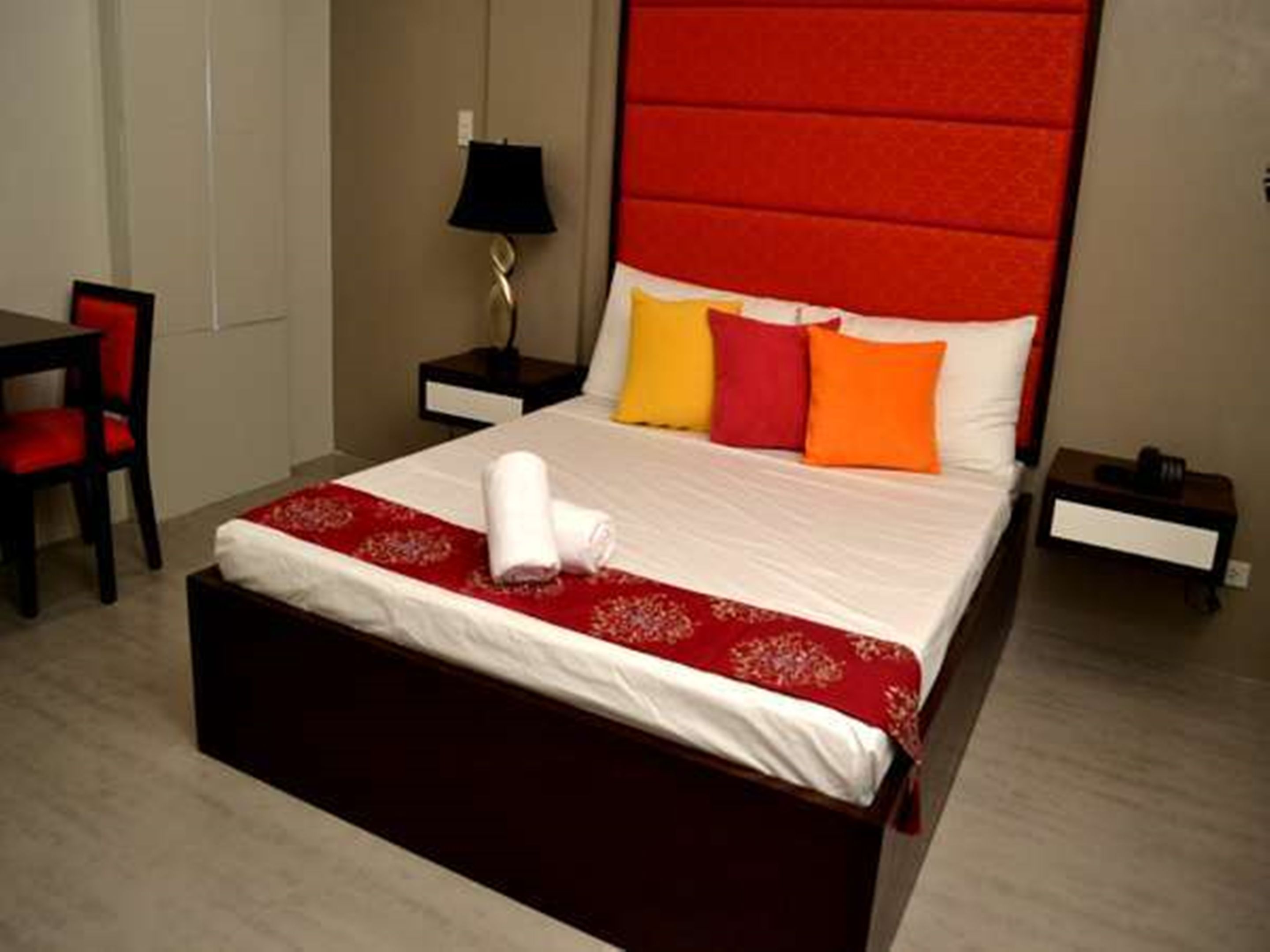 Una habitación de hotel con una cama grande, una mesita de noche, una lámpara y una silla.