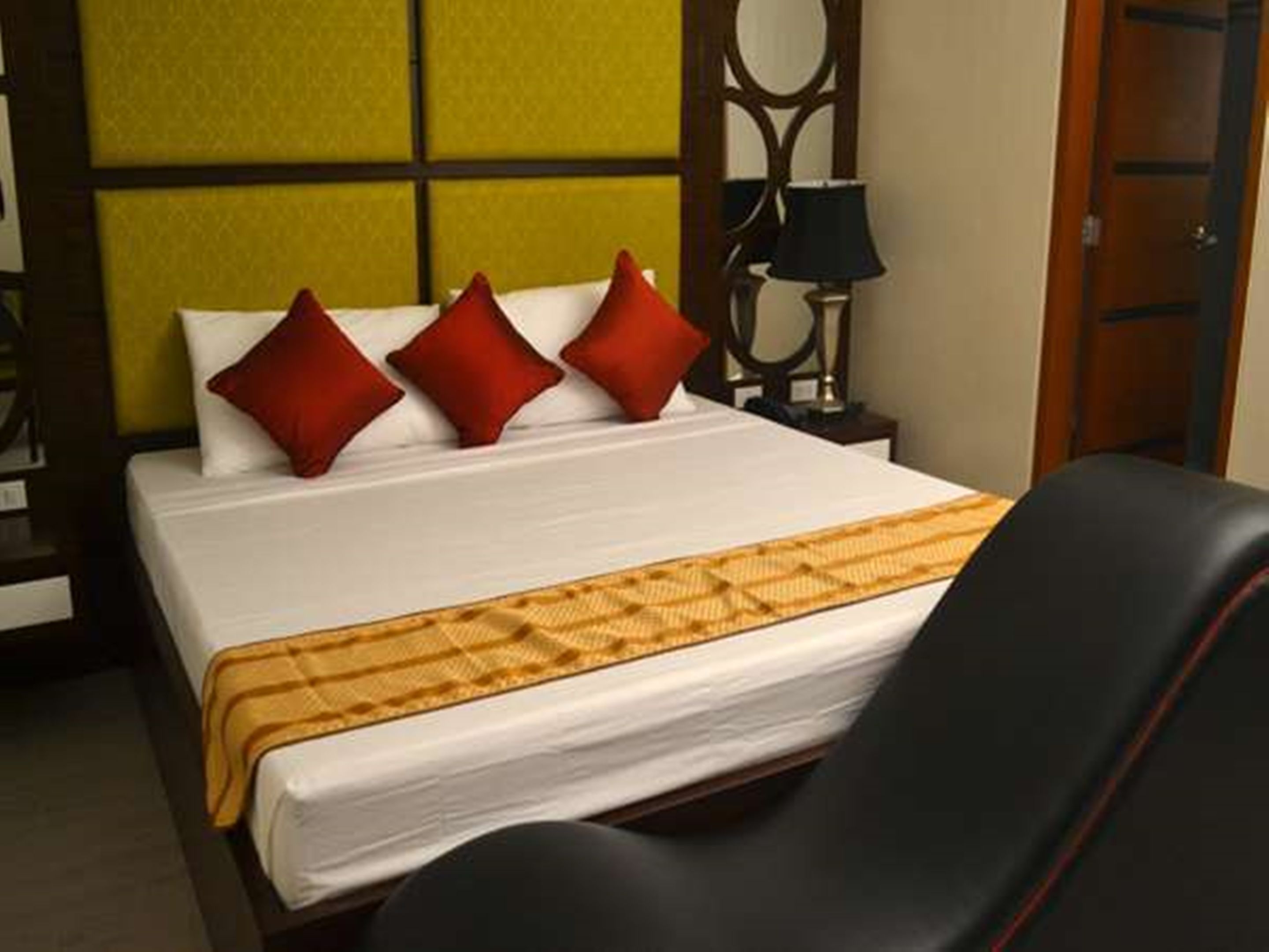 A hotel room with a bed, a nightstand, a lamp, and a door.