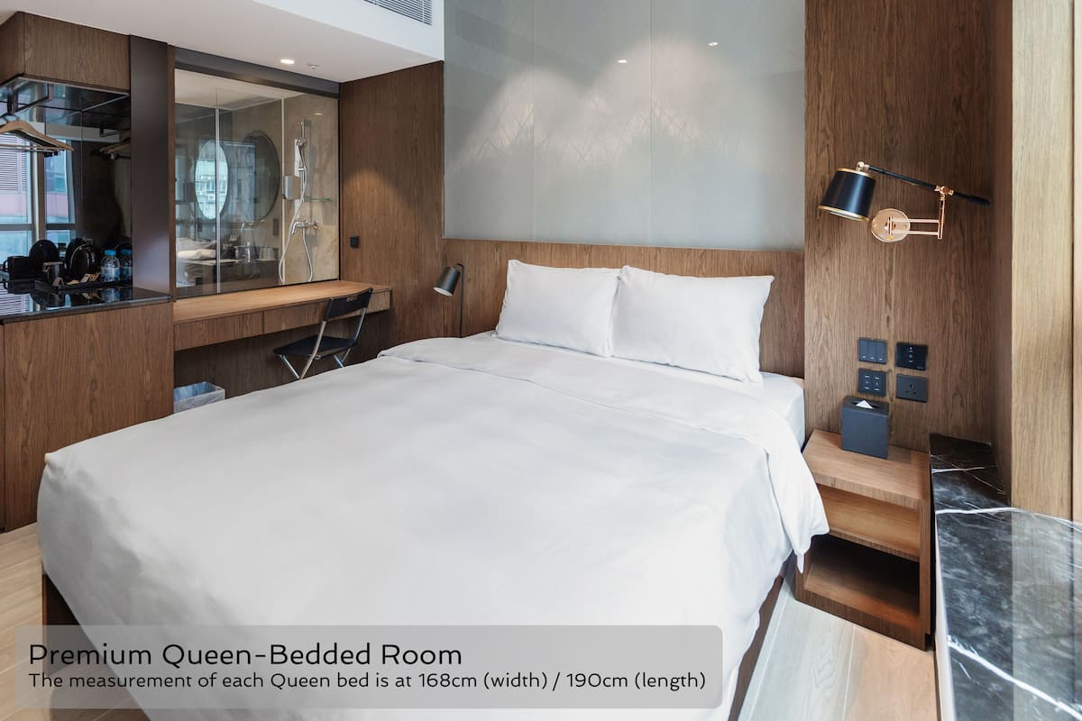 A premium queen-bedded room with a bed measuring 168cm by 190cm, a wooden headboard, a bedside table with a lamp, and a mirror.