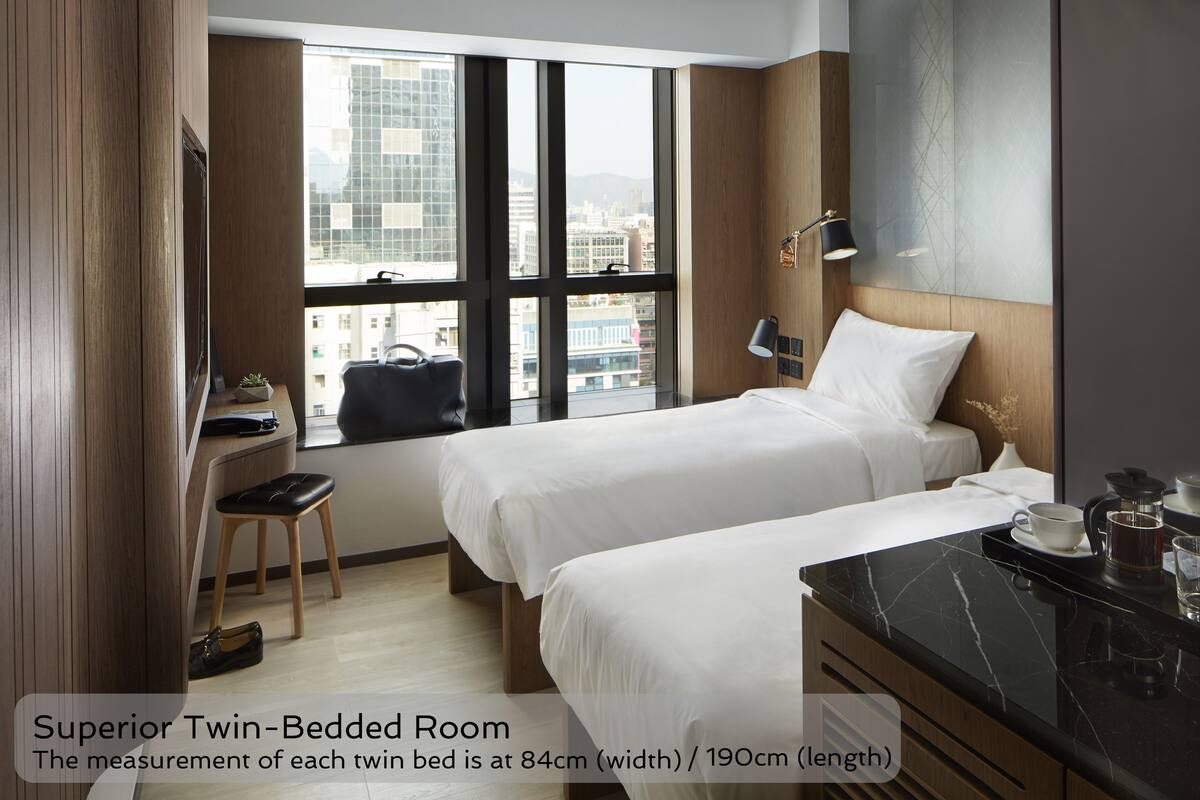 A Superior Twin-Bedded Room with two beds, a desk, a chair, and a view of the city through large windows.
