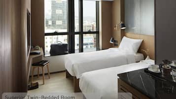 A Superior Twin-Bedded Room with two beds, a desk, a chair, and a view of the city through large windows.