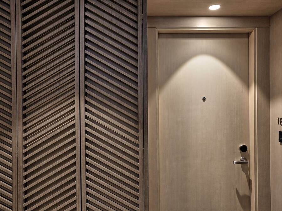 A modern hotel room with a wooden slatted wall, a plain door with a number plate, and a recessed ceiling light.