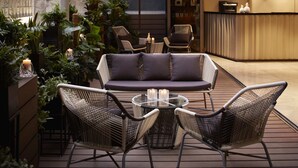 A cozy outdoor seating area with wicker chairs and a cushioned sofa, surrounded by lush greenery and candles. - The Otto Hotel (Kowloon)