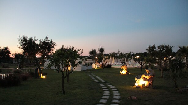 A garden with a paved path, trees, and a fire pit area. - Tenuta Donna Caterina (Mesagne)