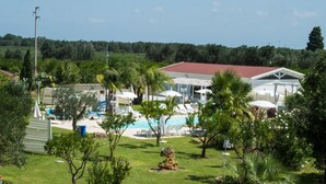 A pool area with lounge chairs and umbrellas, surrounded by greenery and a building with a red roof. - Tenuta Donna Caterina (Mesagne)