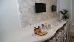 A breakfast bar with a white countertop, two televisions mounted on the wall, and a vase with flowers on the right. - Landlord in Trastevere (Rome)
