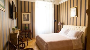 A hotel room with a large bed, a desk with a chair, a television, and a framed picture on the wall. - Landlord in Trastevere (Rome)