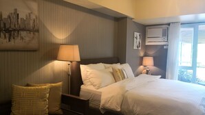 Habitación de hotel con cama, dos lámparas de noche, aire acondicionado instalado en la pared y ventana con cortinas.