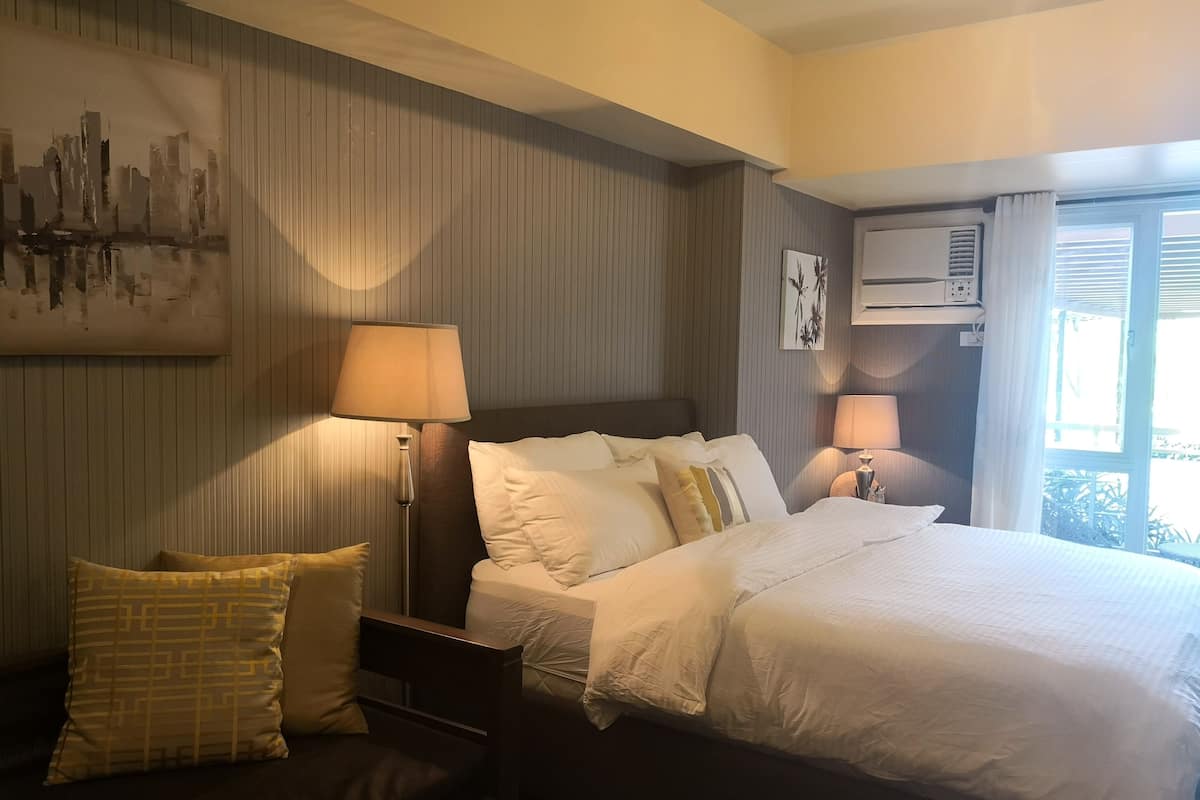 Ein Hotelzimmer mit einem Bett, zwei Nachttischlampen, einer Wandklimaanlage und einem Fenster mit Vorhängen.