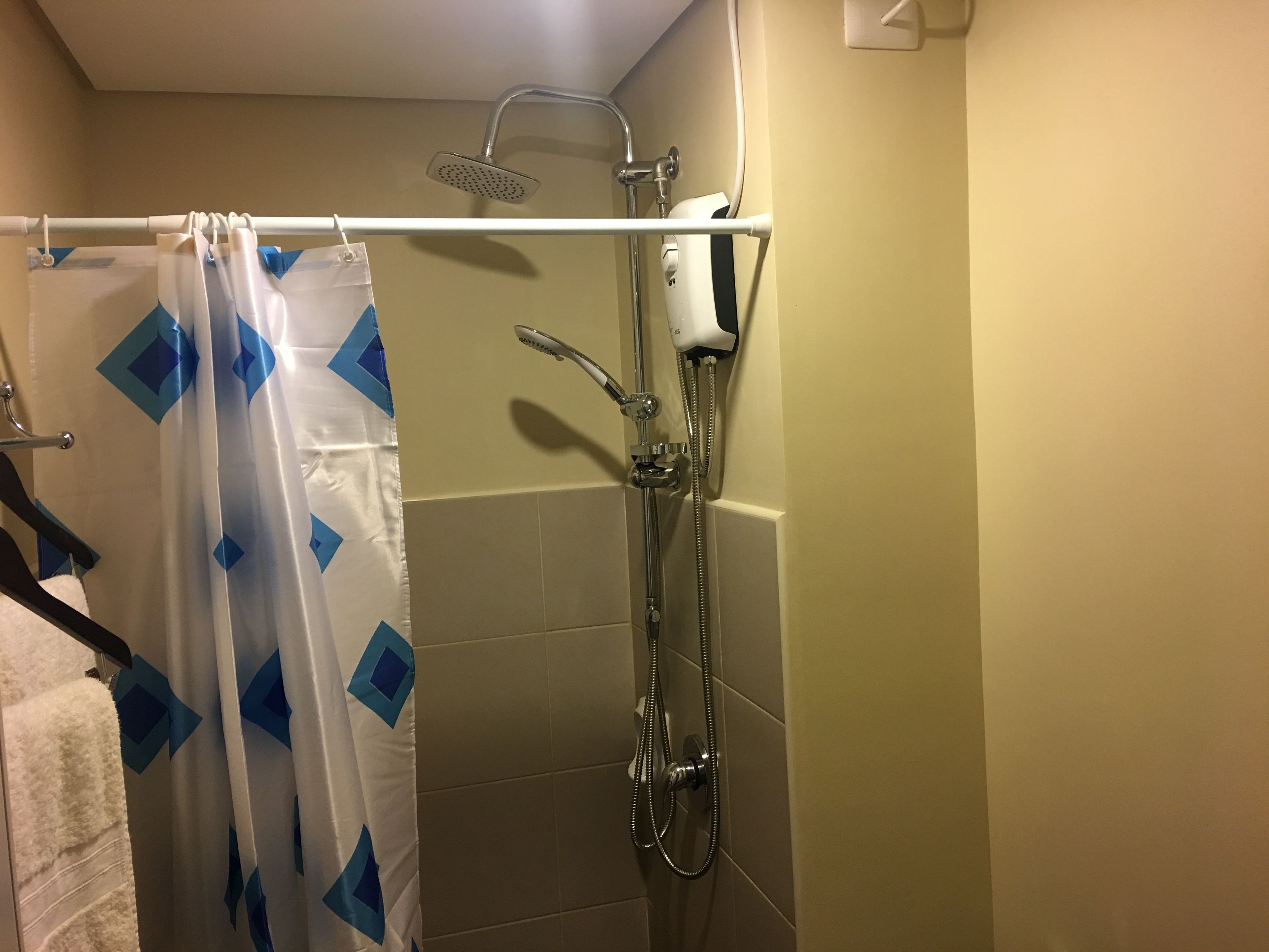 A shower area with a handheld showerhead, a wall-mounted faucet, and a shower curtain with a geometric pattern.