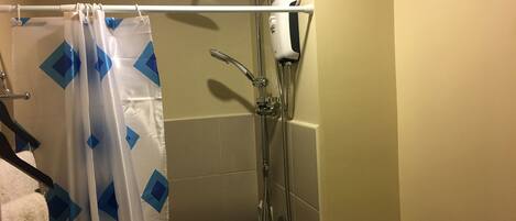 A shower area with a handheld showerhead, a wall-mounted faucet, and a shower curtain with a geometric pattern.