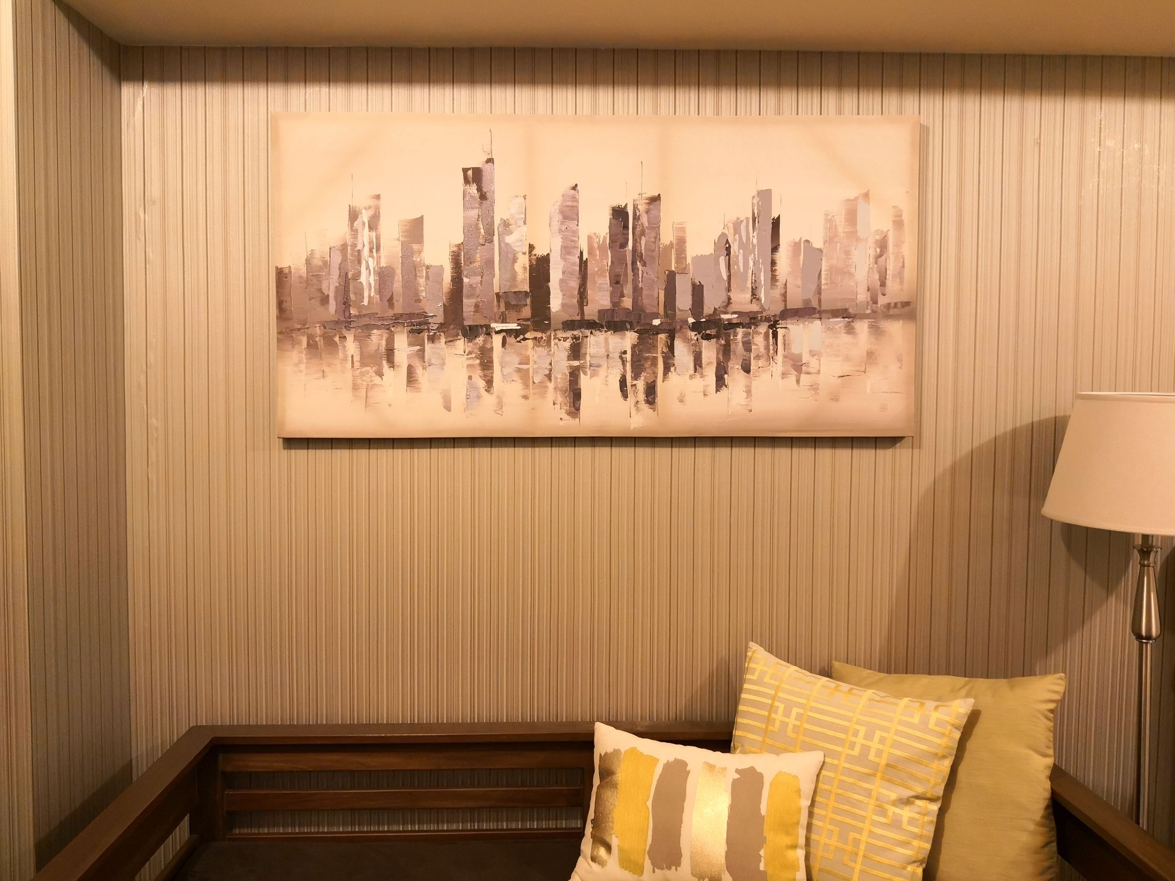 A hotel room with a cityscape painting on the wall, a wooden bench, and two pillows.