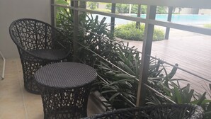 Un balcón con muebles de mimbre, vistas a una piscina y abundante vegetación.
