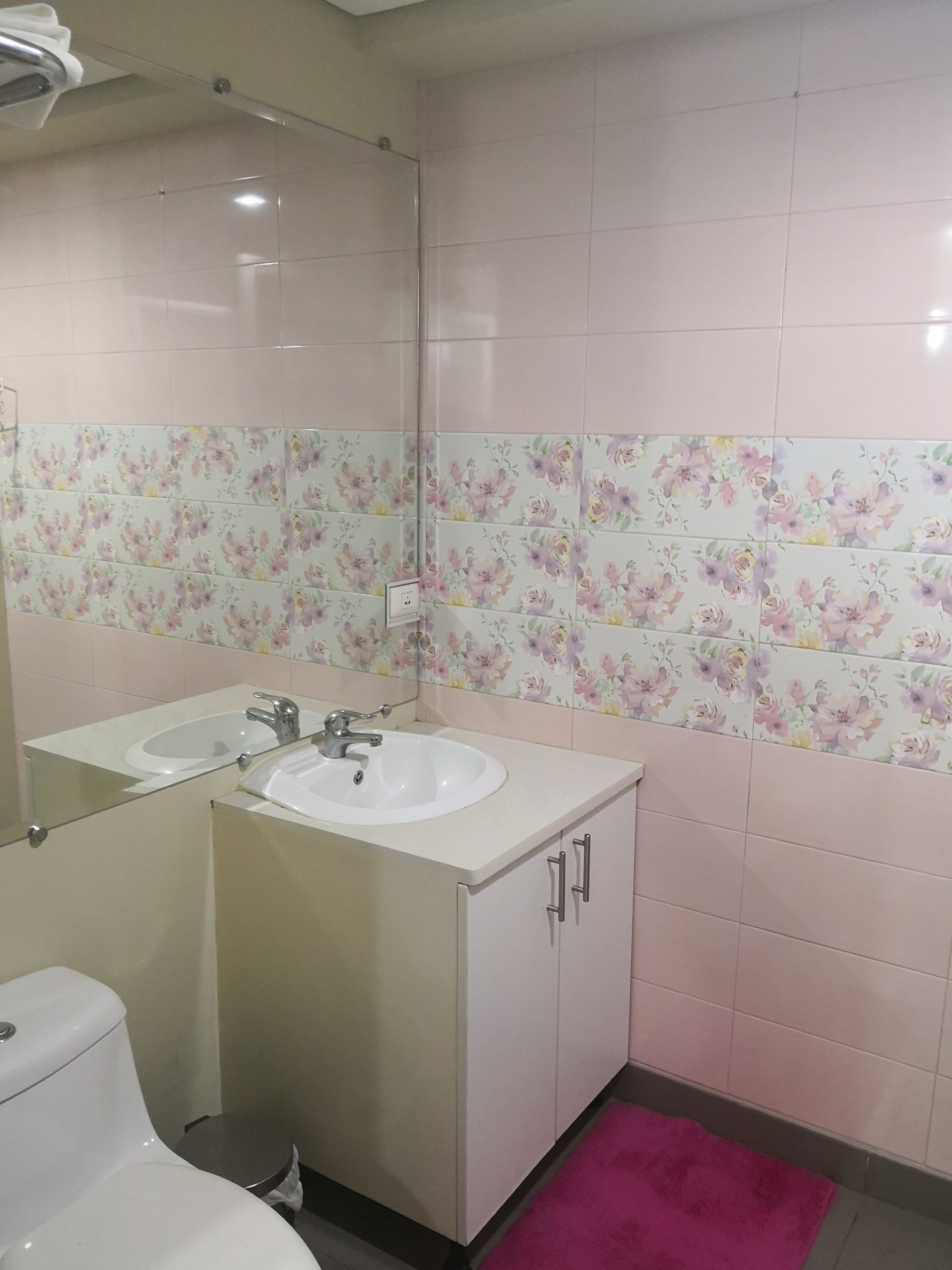 A bathroom with a white sink, a mirror, and a toilet. The walls are tiled with floral patterns.
