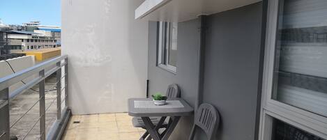 A balcony with a small table and two chairs, a potted plant, and a window.