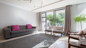 Een moderne woonkamer met een grijze bank, een houten salontafel en een groot raam met gordijnen.