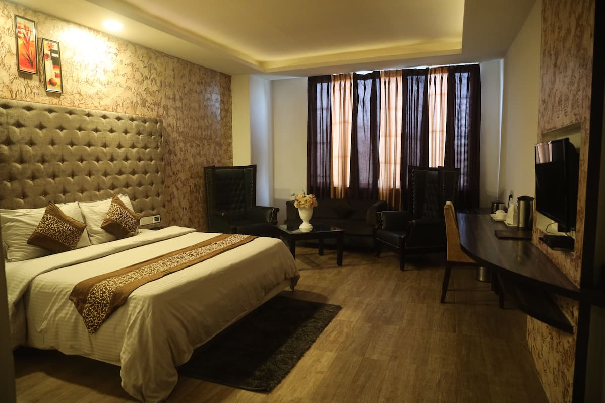 A hotel room with a large bed, a desk, a TV, and a window with curtains.