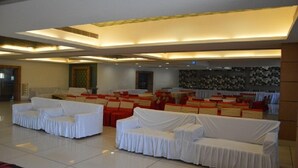 A spacious hall with rows of white-covered sofas and red cushions, a high ceiling with recessed lighting, and a patterned wall in the background. - The Royal Paradise (Karnal)