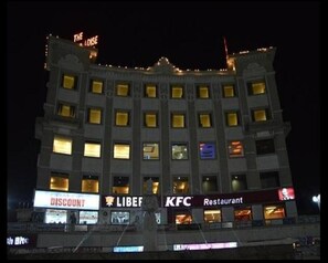 Un hotel de varios pisos con señalización iluminada que dice 'The Oasis' en la parte superior, 'DESCUENTO' en la planta baja, y los restaurantes 'LIBEF' y 'KFC' en el segundo piso.