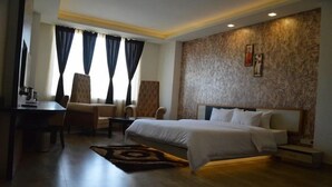 A hotel room with a bed, two armchairs, a desk, and a patterned rug. - The Royal Paradise (Karnal)