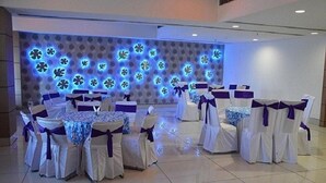 A banquet hall with round tables and chairs, each with white tablecloths and purple sashes. - The Royal Paradise (Karnal)