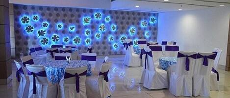 Un salón de banquetes con mesas redondas y sillas, cada una con mantel blanco y fajas moradas.