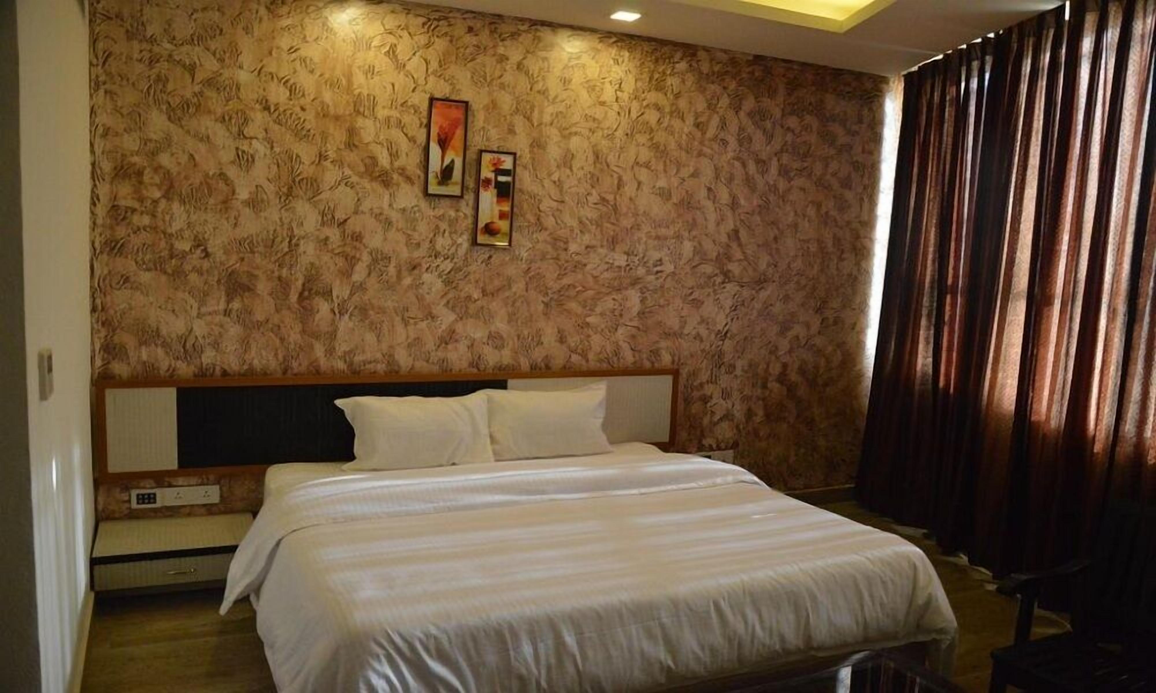 Una habitación de hotel con una cama grande, un cabecero, una mesita de noche y una pared con estampado floral.