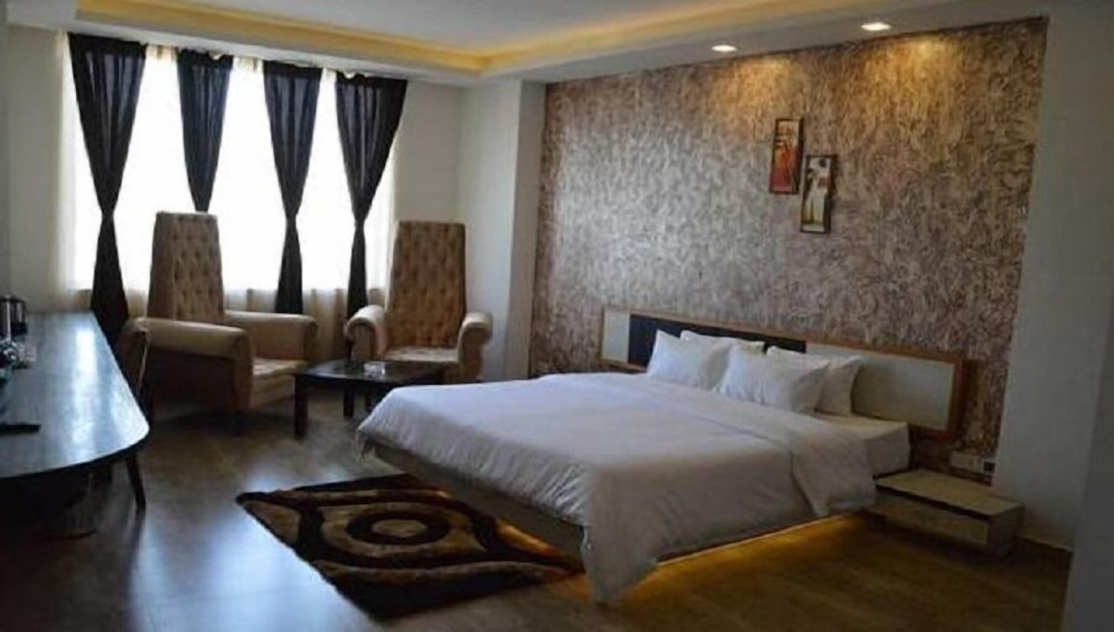 Ein Hotelzimmer mit einem großen Bett, zwei Sesseln, einem kleinen Tisch und einem Schreibtisch.