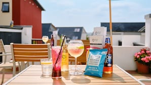 A table with drinks, a bottle of beer, a bag of chips, and a bottle of malt vinegar. - Kilbirnie Hotel (Newquay)