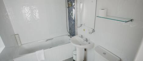 Um banheiro moderno com banheira, pia, vaso sanitário e prateleira de vidro.
