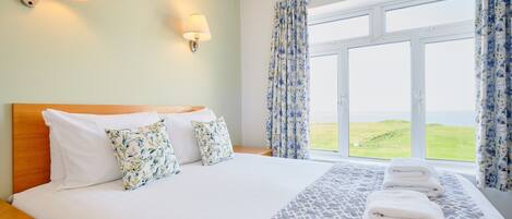 Habitación de hotel con una cama grande, dos lámparas de pared, una ventana con cortinas y vistas al exterior.