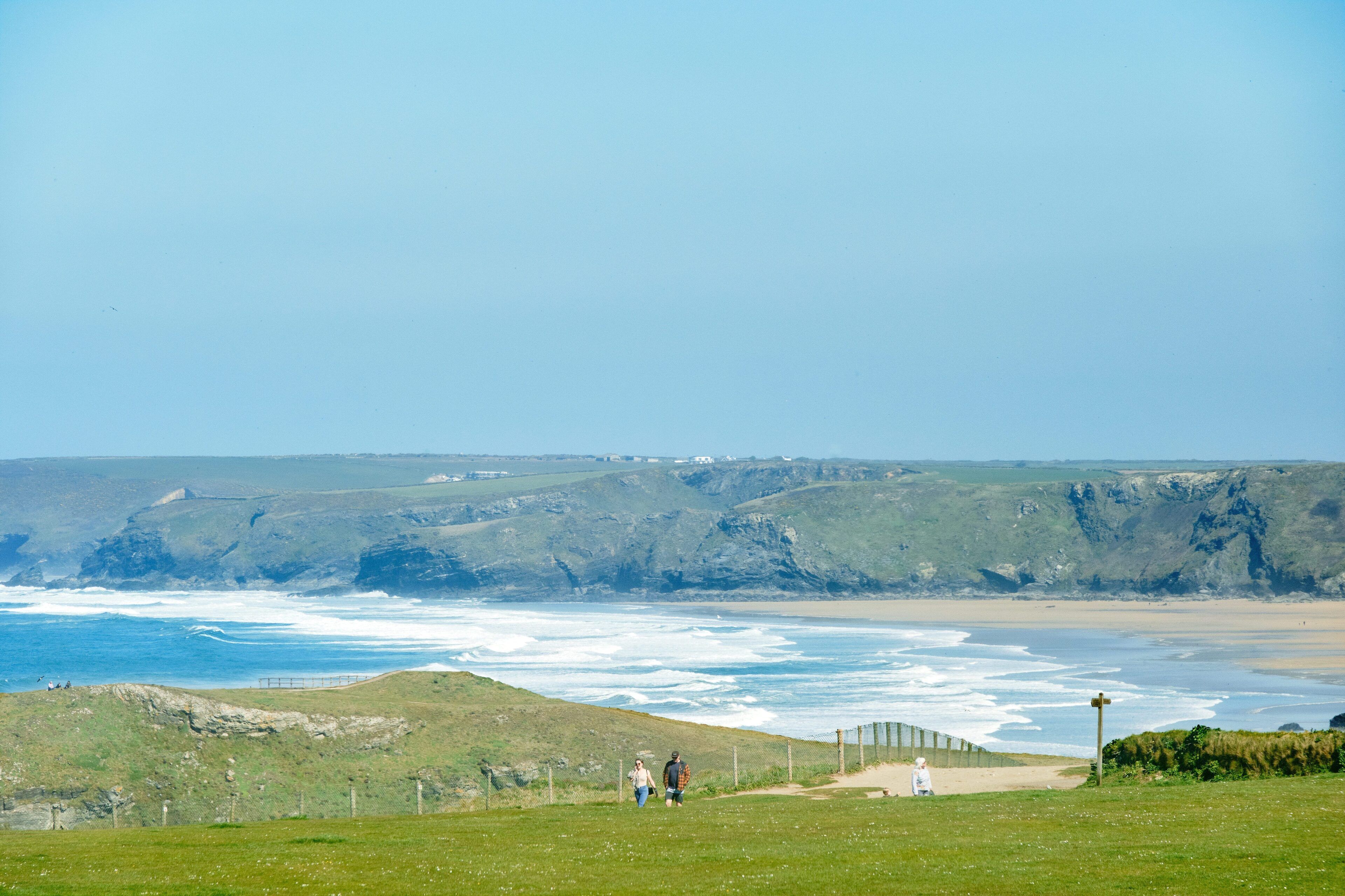 A coastal landscape with grassy hills, a beach, and the ocean.