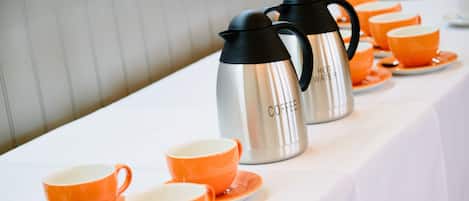 A table set with orange cups and saucers, and two stainless steel hot water carafes labeled "HOT WATER" and "COFFEE".