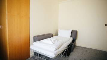 Une petite chambre avec un lit simple, une porte en bois, une tête de lit grise et un matelas blanc.