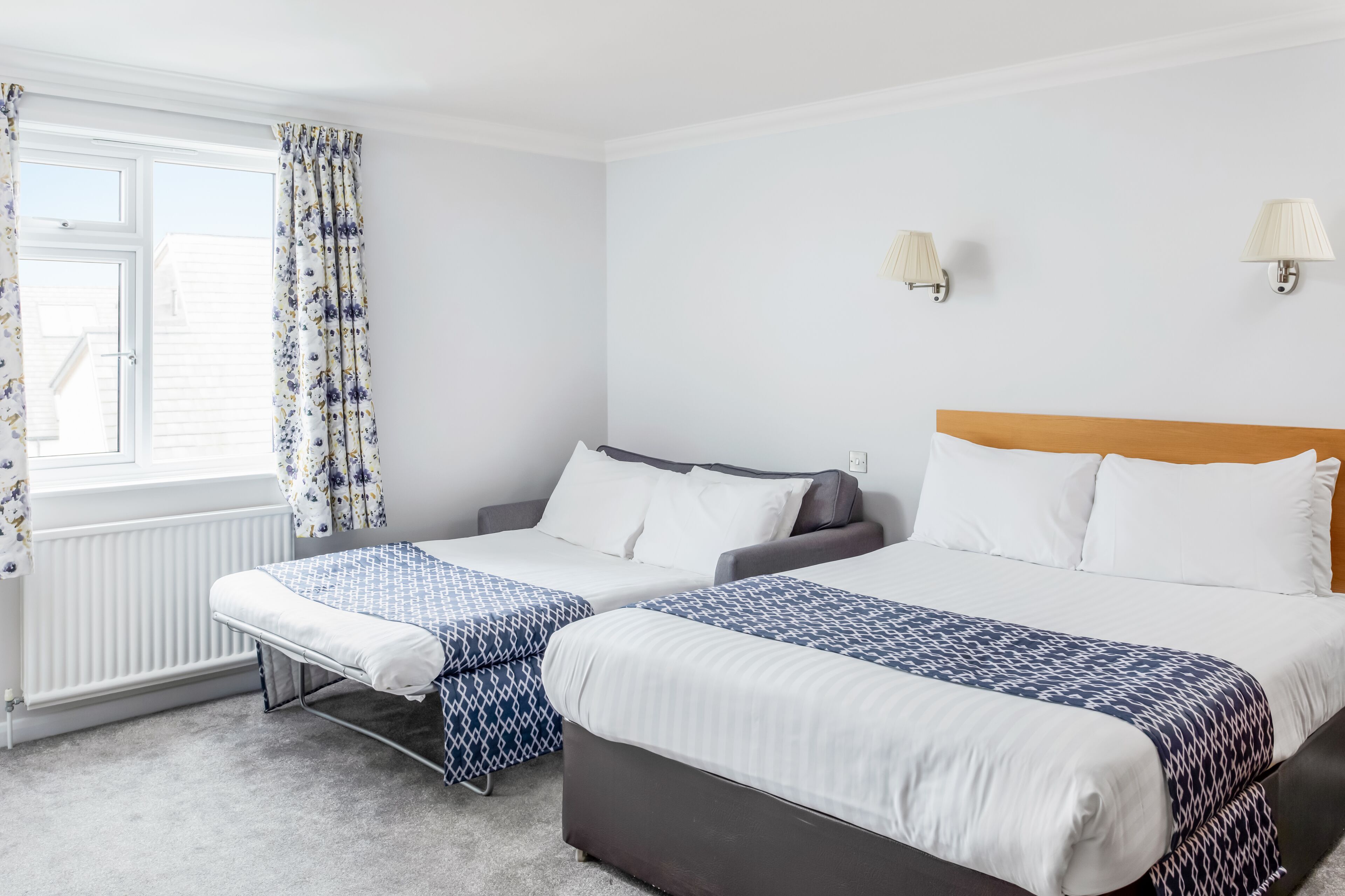 Una habitación de hotel con dos camas, una ventana con cortinas, un radiador y lámparas fijadas a la pared.