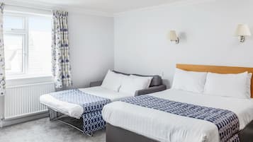 Una habitación de hotel con dos camas, una ventana con cortinas, un radiador y lámparas fijadas a la pared.