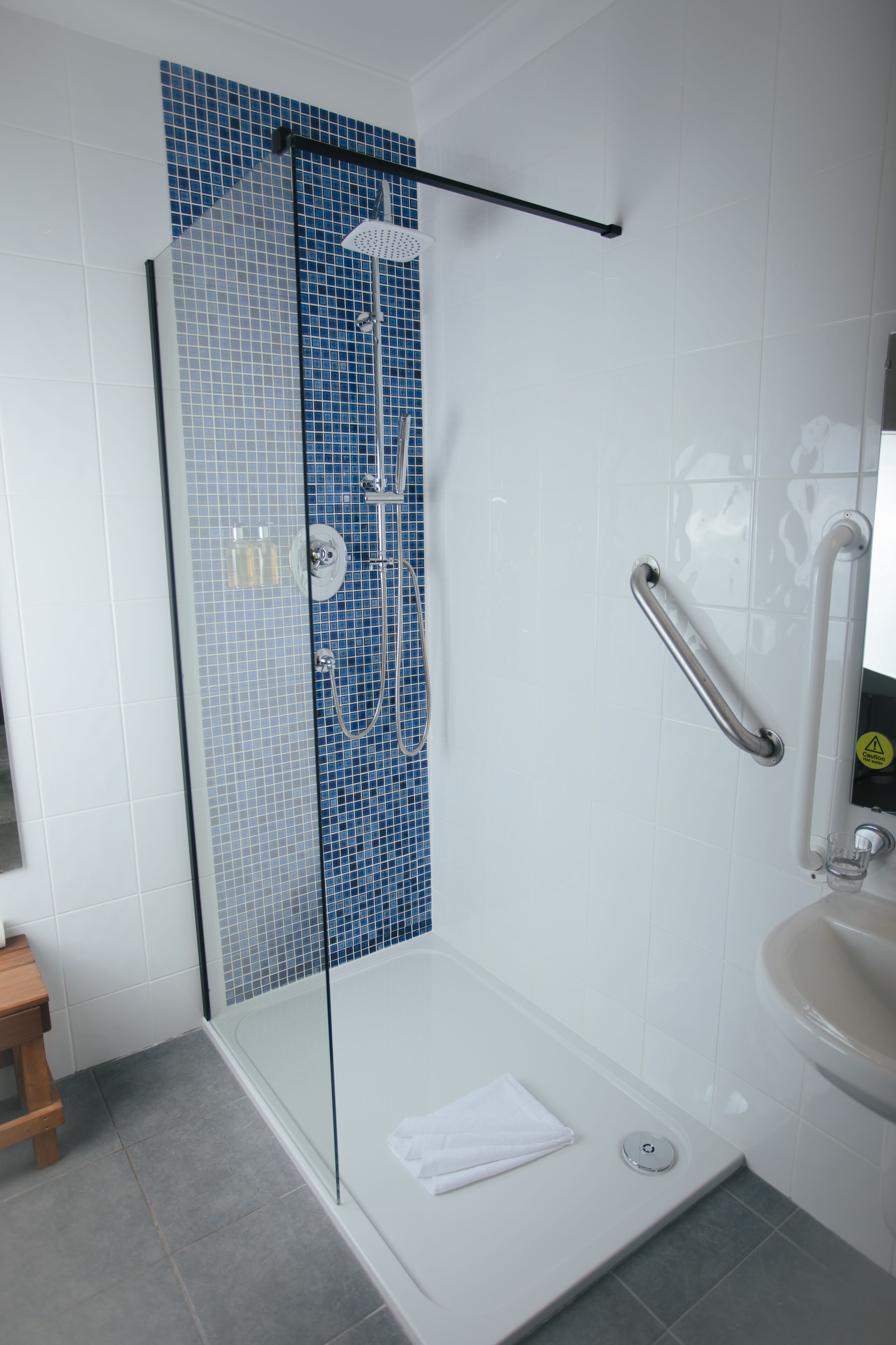 Un baño moderno con ducha de vidrio, un lavamanos blanco y un taburete de madera.
