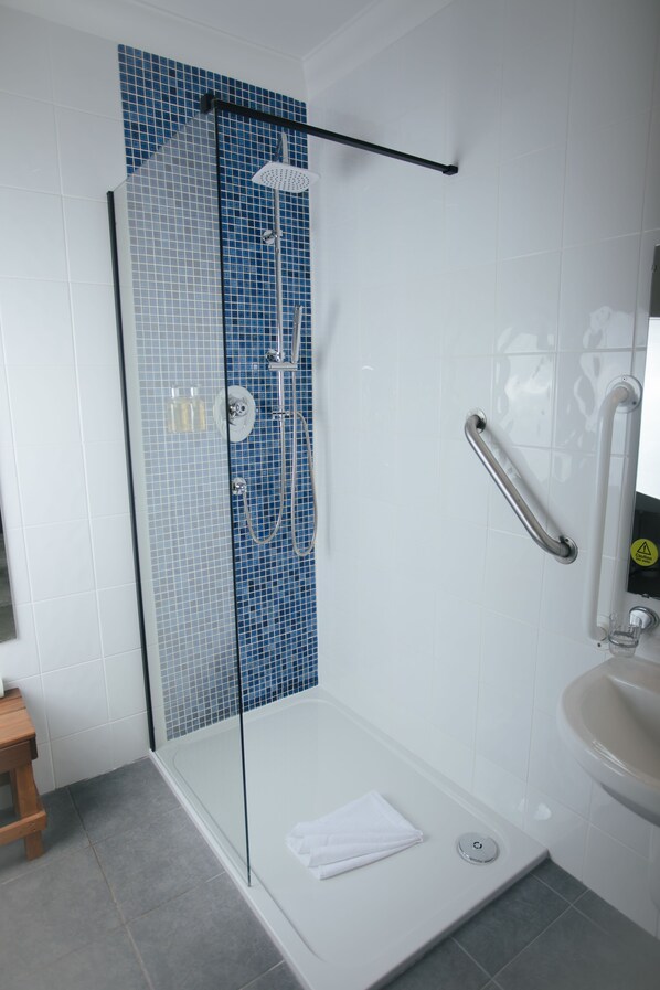 A modern bathroom with a glass-enclosed shower, a white sink, and a wooden stool. - Kilbirnie Hotel (Newquay)