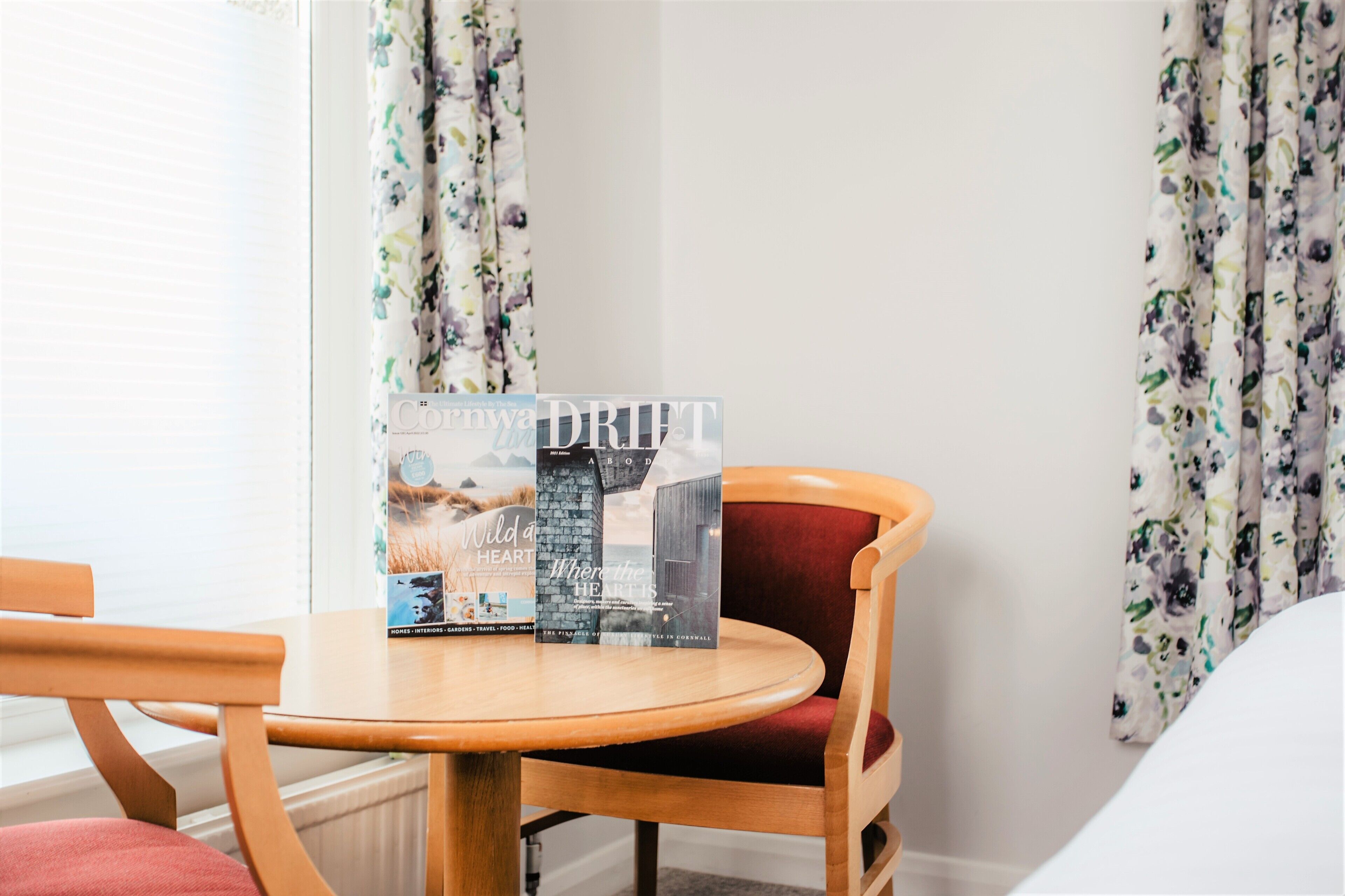 A hotel room with a round wooden table, a red cushioned chair, and a brochure on the table.