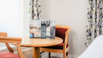 A hotel room with a round wooden table, a red cushioned chair, and a brochure on the table.