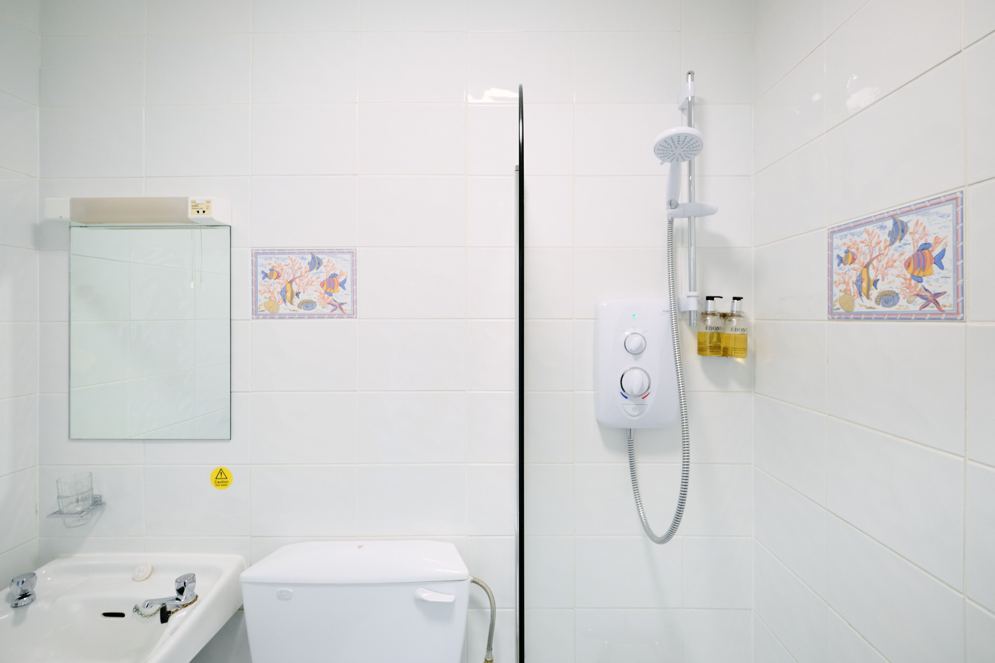 A bathroom with a sink, toilet, and shower. There are decorative tiles and a mirror on the wall.